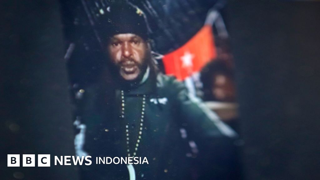An armed Papuan man in front of a Morning Star flag