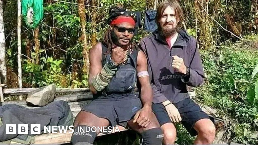 An armed Papuan man stands beside a foreign man in the forest