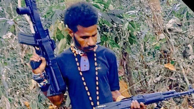 A man holds a long-barreled rifle against a forest backdrop